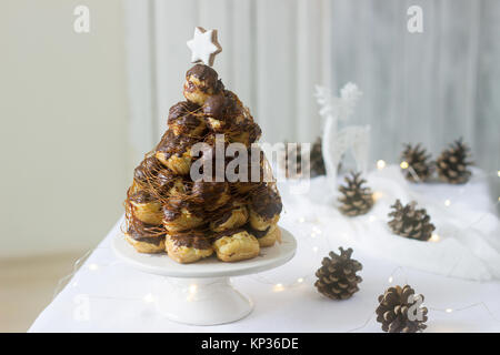 Croquembusch cake in Christmas or New Year decoration with a garland of fir cones and a deer figure. Selective focus. Stock Photo