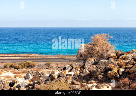 Coastline road, pile of colorful volcanic rocks on edge of desert dune park, Fuerteventura, Canary Islands, Spain . Stock Photo