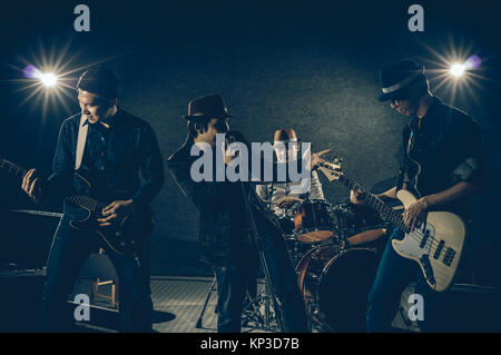 Musician band hand holding the microphone and singing a song and playing music instrument with Fellow band musicians on black background with spot lig Stock Photo