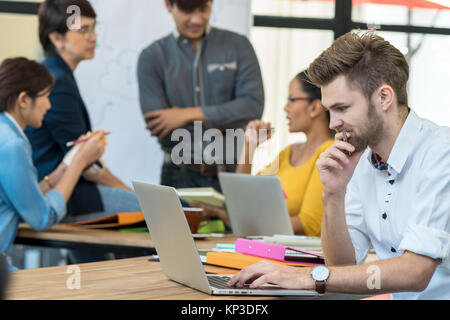 Businessman working in happy action with computer over the photo blurred of Group Of Asian and Multiethnic Business people with casual suit in the mod Stock Photo