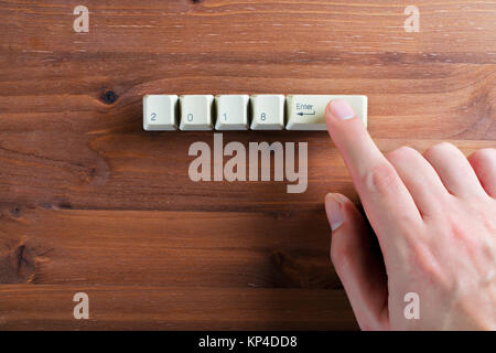 Index finger presses on the keyboard, on which is written 2018 and enter ket on a wooden background. New year 2018 card. Stock Photo