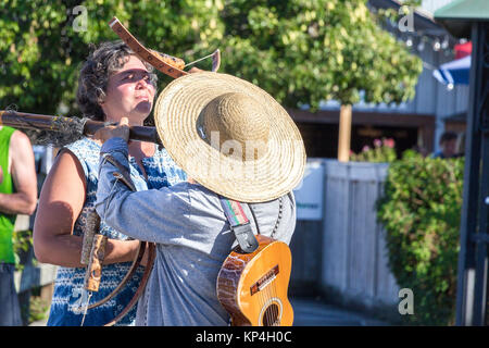 Salt Spring Island, Canada - August 29th, 2017: A man is playing a bamboo flute and an arch for a female tourist at Salt Spring Harbour. Stock Photo
