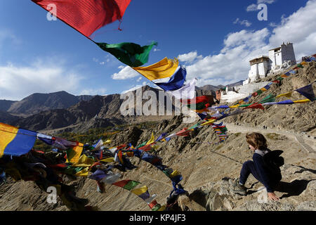 Young caucasian boy sitting on a rock under prayer flags with Tsemo Gompa in the background, Leh, Ladakh, Jammu and Kashmir, India. Stock Photo