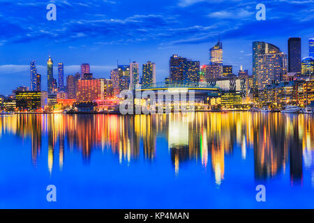 Bright iilluminated waterfront urban architecture of Docklands suburbs in Melbourne reflecting in still waters of Yarra river at sunset. Stock Photo