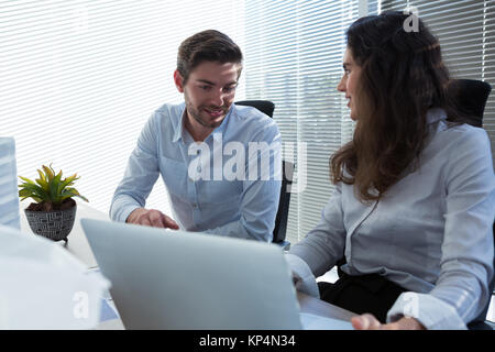 Male and female executives discussing over laptop in office Stock Photo