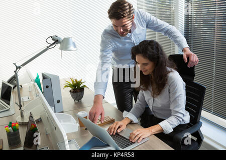 Male and female executives discussing over laptop in office Stock Photo