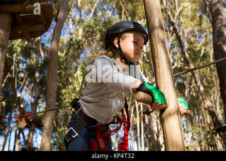 Little girl wearing helmet lining on wooden ladder in the forest Stock Photo