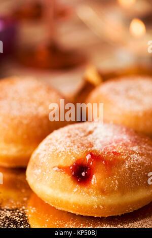 closeup of some sufganiyot, Jewish donuts filled with strawberry jelly traditionally eaten on Hanukkah, and some lit candles on a set table Stock Photo