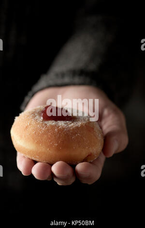 closeup of a sufganiyah, a Jewish donut filled with strawberry jelly traditionally eaten on Hanukkah, in the hand of a man Stock Photo