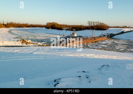 A boat on a frozen river supports the pontoon for crossing to the other shore Stock Photo