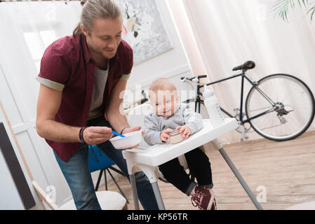 happy father feeding his smiling son with baby food at home Stock Photo