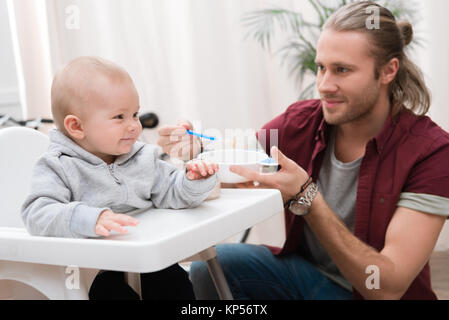 father feeding his cheerful son with baby food at home Stock Photo