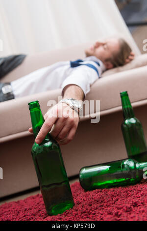 Drunk man sleeping on a sofa and holding bottle of beer Stock Photo