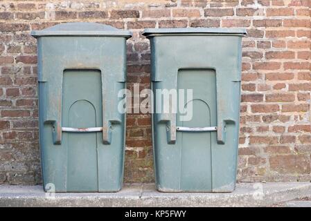 Two old green trash bins beside an old red brick wall Stock Photo