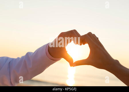 Sonnenaufgang am Strand, Paar formt Herz mit Haenden - sunset at the beach, couple makes a heart with hands Stock Photo