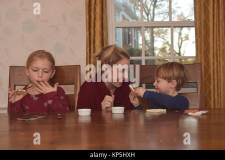 mother sitting with 2 children decorating cookies Stock Photo