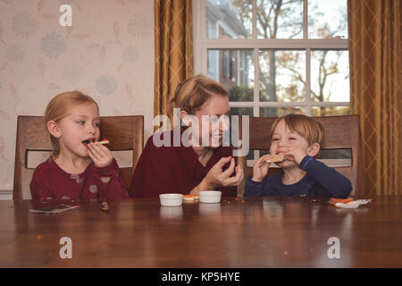 mother sitting with 2 children decorating cookies Stock Photo