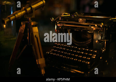 Small vintage telescope standing on the wooden table next to old dark typewriter Stock Photo