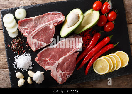 Raw porterhouse beef steak with ingredients close-up on the table. Horizontal top view from above Stock Photo