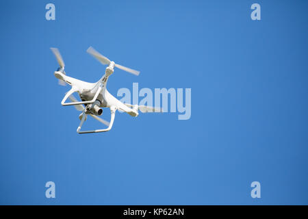 White photography drone in flight against a clear blue sky Stock Photo