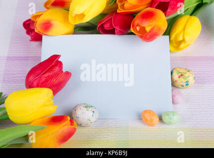 Easter candy and tulips around a blank envelope on a colorful tabletop Stock Photo