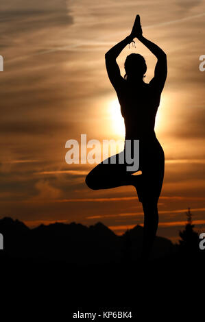 Silhouette of a woman practicing yoga against the light of the evening sun. Vrksasana, tree pose. French Alps. France. Stock Photo