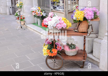 A cart with over wicker baskets and an old wicker fishing basket full of flowers for sale Stock Photo