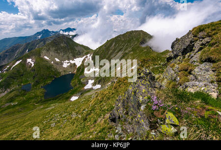 edge of steep slope on rocky hillside in cloudy weather. dramatic scenery with snow near glacier in Fagaras mountains Stock Photo