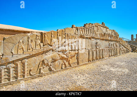 The ruined facade wall of the ancient palace of Xerxes (Hadish) with preserved reliefs, including classical Persian themes - lion and bull, soldiers a Stock Photo