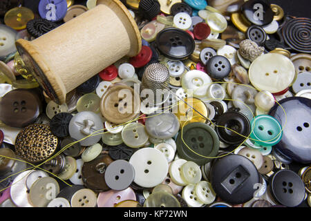 Close up of yellow thread in silver needle with thimble and bobbin on buttons . Stock Photo