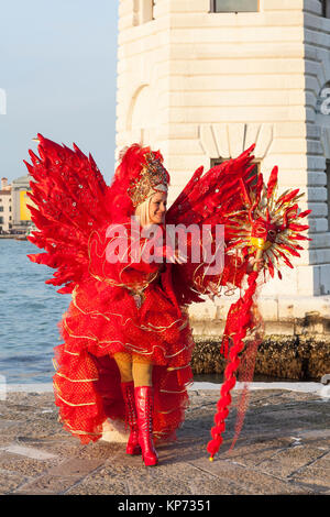 Venice Carnival 2017, Veneto, Italy woman in red Satan costume with wings ans staff posing at sunset at the lighthouse on San Giorgio maggiore Stock Photo