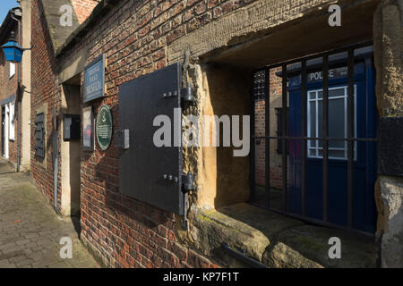 Close-up of barred window, shutter, signs & entrance to historic jail, now the Prison and Police Museum - Ripon, North Yorkshire, England, UK. Stock Photo