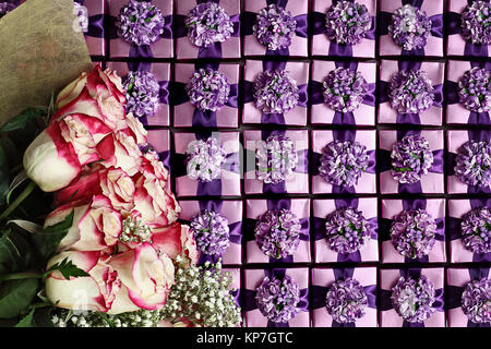 Flat lay of long stem pink and white roses over a background of violet color gift boxes with pretty bows. Stock Photo