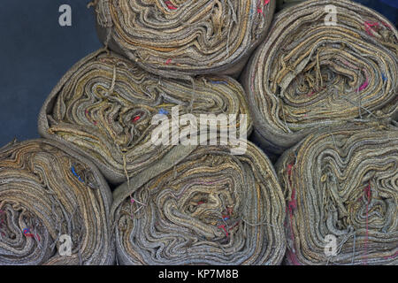 Empty canvas bags twisted into bobbins lie a mountain near the wall of blue color. Stock Photo