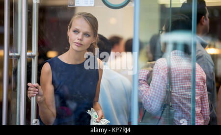 Pretty, young woman leaving a store/restaurant with cash in her hand after having paid for for the goods/food Stock Photo