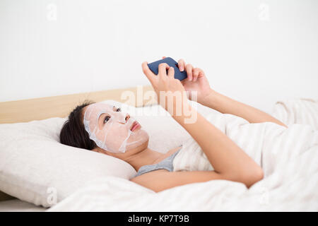Woman playing game with smartphone in bed when using the paper mask Stock Photo
