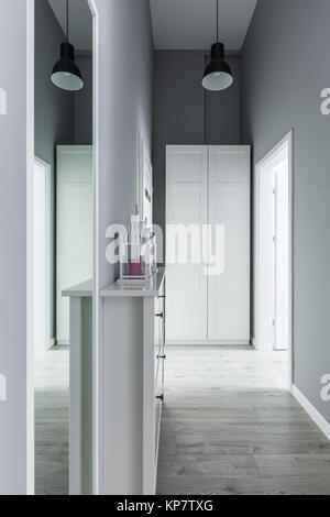 High and narrow gray hallway with white wardrobe and mirror Stock Photo