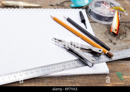 writing-book with fishing tackles and design tools on wooden board Stock Photo