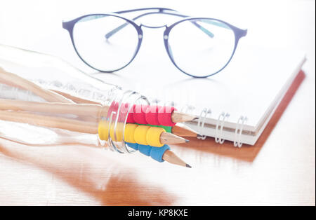 Pencils in bottle with eyeglasses on notebook Stock Photo