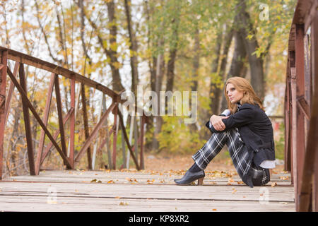 Sad girl sitting on a bridge in the forest Stock Photo