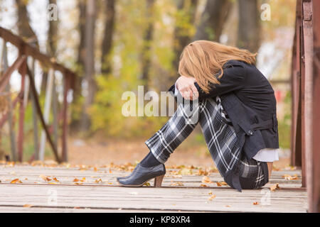 Sad girl sitting on a bridge with her head resting on his knees Stock Photo