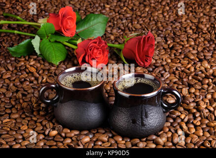 Two cups of black coffee on the background from the coffee beans and a red roses. Stock Photo