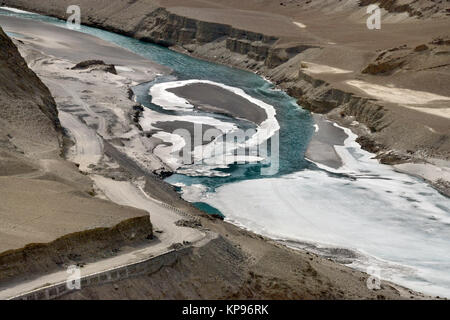 The confluence of the rivers Indus and Zanskar in winter, the canal is covered with ice, aquamarine water is visible, along the port side there is a c Stock Photo