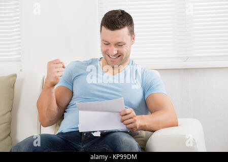 Man Clenching Fist While Reading Letter On Sofa Stock Photo
