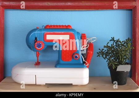 Toy and vintage sewing machine on blue background with pot of plant Stock Photo