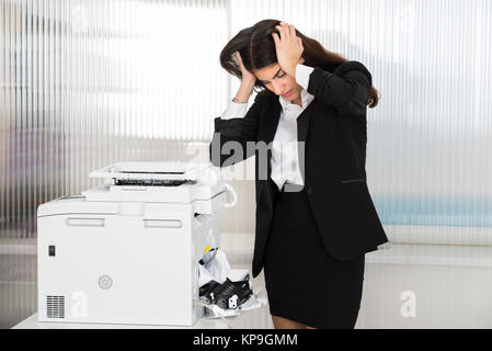 Irritated Businesswoman Looking At Paper Stuck In Printer Stock Photo