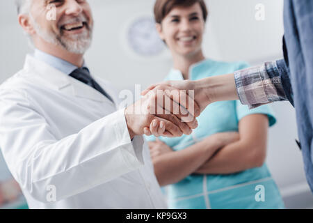 Medical staff welcoming a patient at the clinic: the doctor is giving an handshake and smiling, medical service and healthcare professionals concept,  Stock Photo