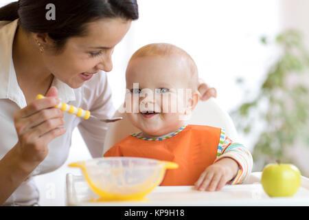 Mother feeding her baby with spoon. Mother giving healthy food to her adorable child at home Stock Photo