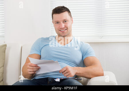 Happy Man Holding Letter On Couch At Home Stock Photo