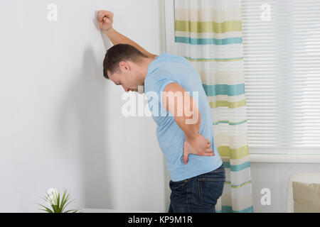 Man Suffering From Backache While Standing Against Wall Stock Photo